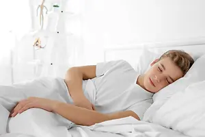 A boy sleeps on a bed with white sheets and pillows