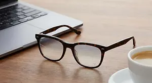 glasses on a table with a laptop and a cup of coffee