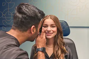 A man doctor using a sphygmomanometer to check the eye pressure of a smiling woman patient