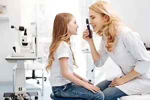 A woman is examining the eye of a little girl in an optometrist's office.