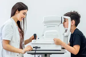 A young boy is having his eye checked by a female doctor using a white machine in a white room