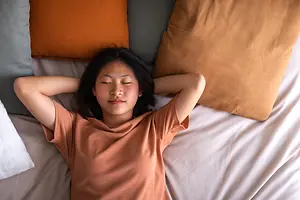 A woman sleeping in a bed with her eyes closed and her head resting on her hands