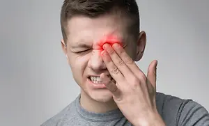 A man appears to be in pain, holding his nose with a red mark on it and his eyes closed