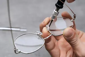 A person holding a pair of glasses with a tool to adjust them.