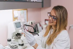 A woman in a lab coat is examining a pair of glasses.
