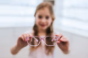 A girl is holding up a pair of pink glasses