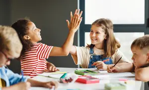 Group of kids sitting at a table and giving high fives