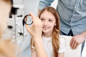 A young girl is having her eyes examined by an optometrist in a medical room.