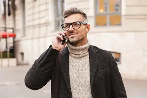 Man wearing glasses and coat on the phone in the street