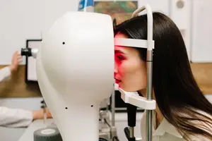 A woman is looking into an ophthalmoscope in a hospital room