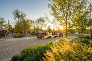 Sunset in a park with people sitting on a bench under a tree and others walking on the sidewalk.