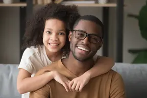 A man and a little girl are sitting on a couch and smiling for the camera.