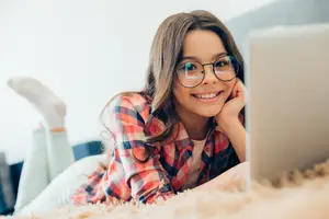 A girl is smiling while lying on the floor with her laptop beside her