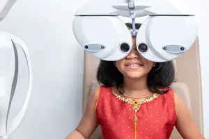 A girl is sitting in a chair and wearing a device on her head, possibly for an eye examination.