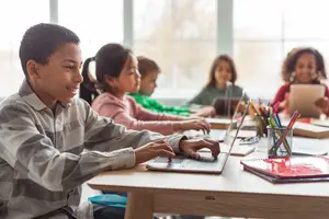 Kids sitting in a classroom and using laptops and tablets