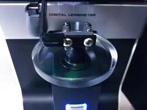 Close-up of a digital lensmeter with a glass lens on a black stand