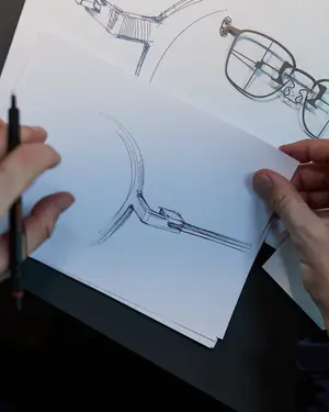 A person is drawing a sketch of a pair of glasses with a pen on a piece of paper.