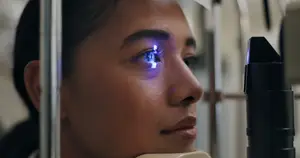 A woman is examining her eye with an ophthalmoscope in a clinic setting.