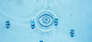 An image of water droplets in a blue water body, with a spiral-shaped water droplet in the center and three small water droplets on the left side. The water droplets are scattered on the water body, and the water droplets are reflecting the light. The image has a blue and white color scheme.
