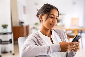 A smiling woman sitting on a chair and holding a phone in her hand.