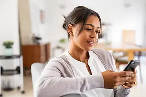 A smiling woman sitting on a chair and holding a phone in her hand.
