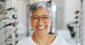 Portrait of an older woman smiling and standing in front of a display of glasses in a shop