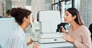 Woman having her eye examined by a woman in a pink sweater in an optometrist's office.