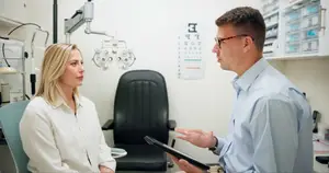 An optometrist consults with a female patient in an office setting, discussing eye health with a tablet in hand.