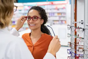 An adult woman is trying on glasses with a doctor in a pharmacy.