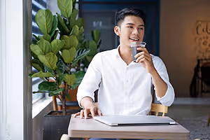 Asian man sitting at a table drinking a cup of coffee