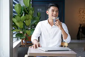 Asian man sitting at a table drinking a cup of coffee