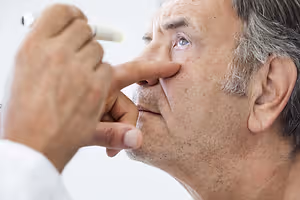 An older man having his eye examined by a doctor using a pen light.