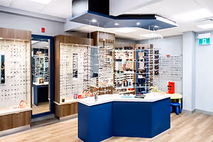 A close-up of an optical shop's interior with a desk full of glasses, shelves with glasses, and a person reflected in a mirror.