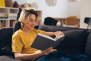A person reading a book on a couch while smiling