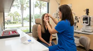A woman is adjusting a female patient's eyeglass frames at a doctor's office.