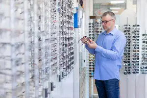 A man in a blue shirt is examining glasses in a store.