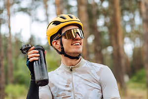 A man is smiling and holding a bottle in the forest