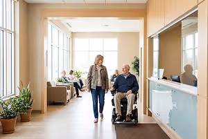 Optometry clinic hallway with a woman walking beside an older man using a motorized wheelchair