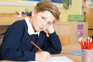 A boy sitting in a classroom writing on a piece of paper