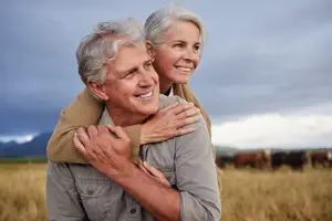 A couple smiling and hugging in a field with cows and a cloudy sky in the background