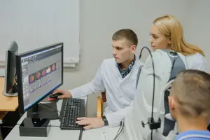 A man and two women are working on a computer monitor with an eye exam machine in front of them.