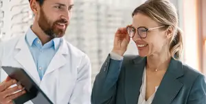 A man and a woman in formal attire standing and smiling while looking at a tablet, possibly in an optical clinic.