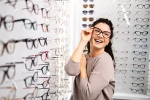 A woman standing in front of a wall of glasses with her hand on her face smiling