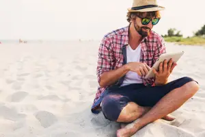 A man sitting on the sand with a tablet