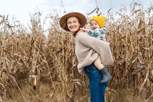 A woman with a hat holds a baby in a corn field