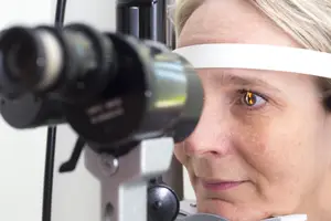 An older woman with blonde hair is having her eyes checked by an optometrist using an eye exam machine