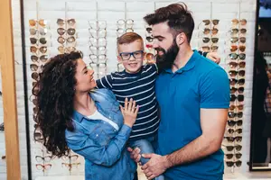 A family of three people smiling at each other while standing in front of a display of glasses in Idaho Falls