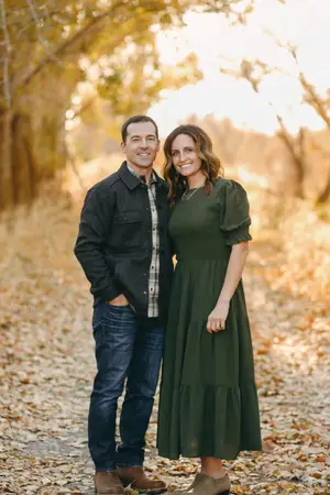 A couple posing for a photo on a sunny day in a forest with dry leaves on the ground