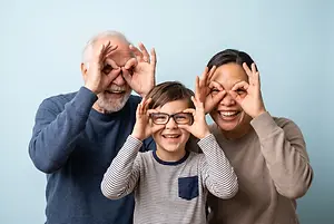 Smiling multigenerational family making circles around their eyes with their hands, while the child wears glasses