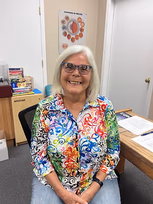 Woman sitting in office chair with colorful shirt and smiling